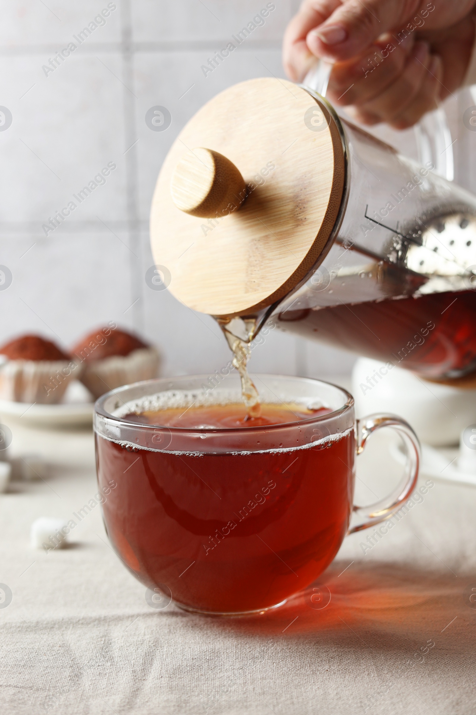 Photo of Woman pouring tea into cup at light table, closeup