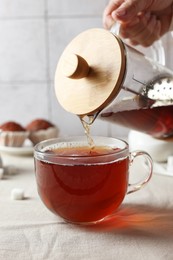 Woman pouring tea into cup at light table, closeup