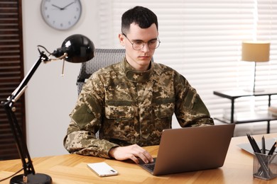 Photo of Military service. Young soldier working with laptop at wooden table in office