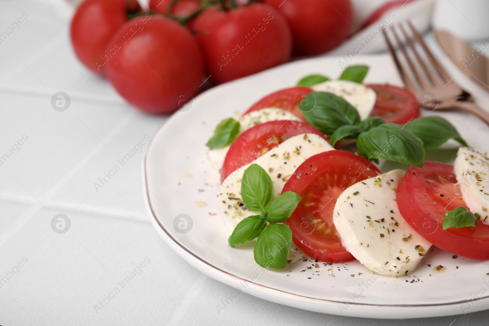 Photo of Caprese salad with tomatoes, mozzarella, basil and spices on white table, closeup