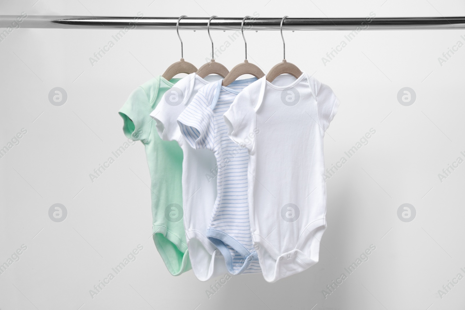 Photo of Baby bodysuits hanging on rack near white wall, closeup