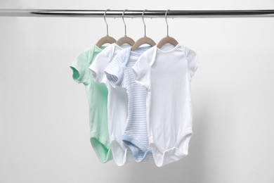 Baby bodysuits hanging on rack near white wall, closeup