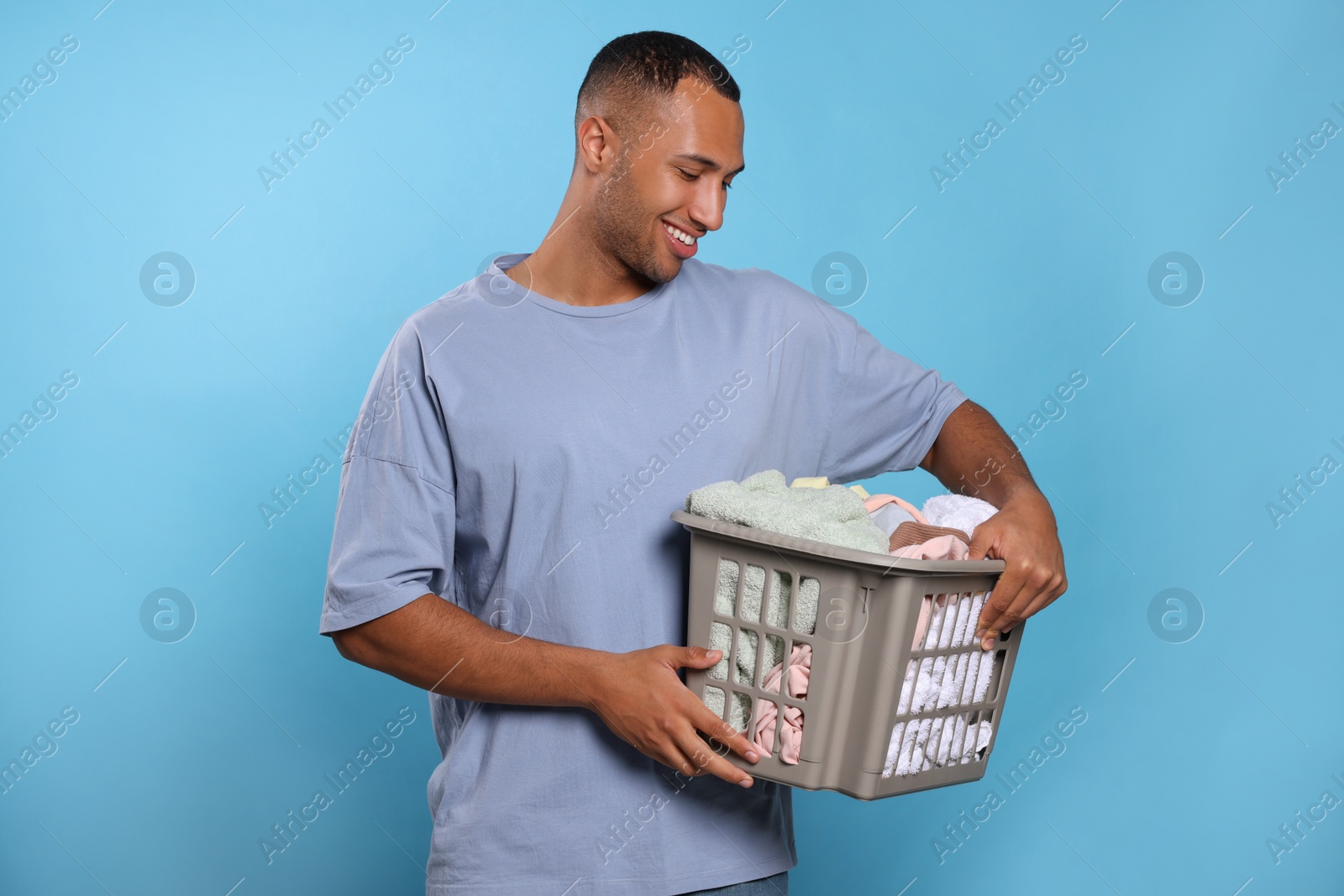 Photo of Happy man with basket full of laundry on light blue background