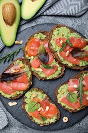 Photo of Delicious sandwiches with salmon, avocado and herbs on grey table, flat lay