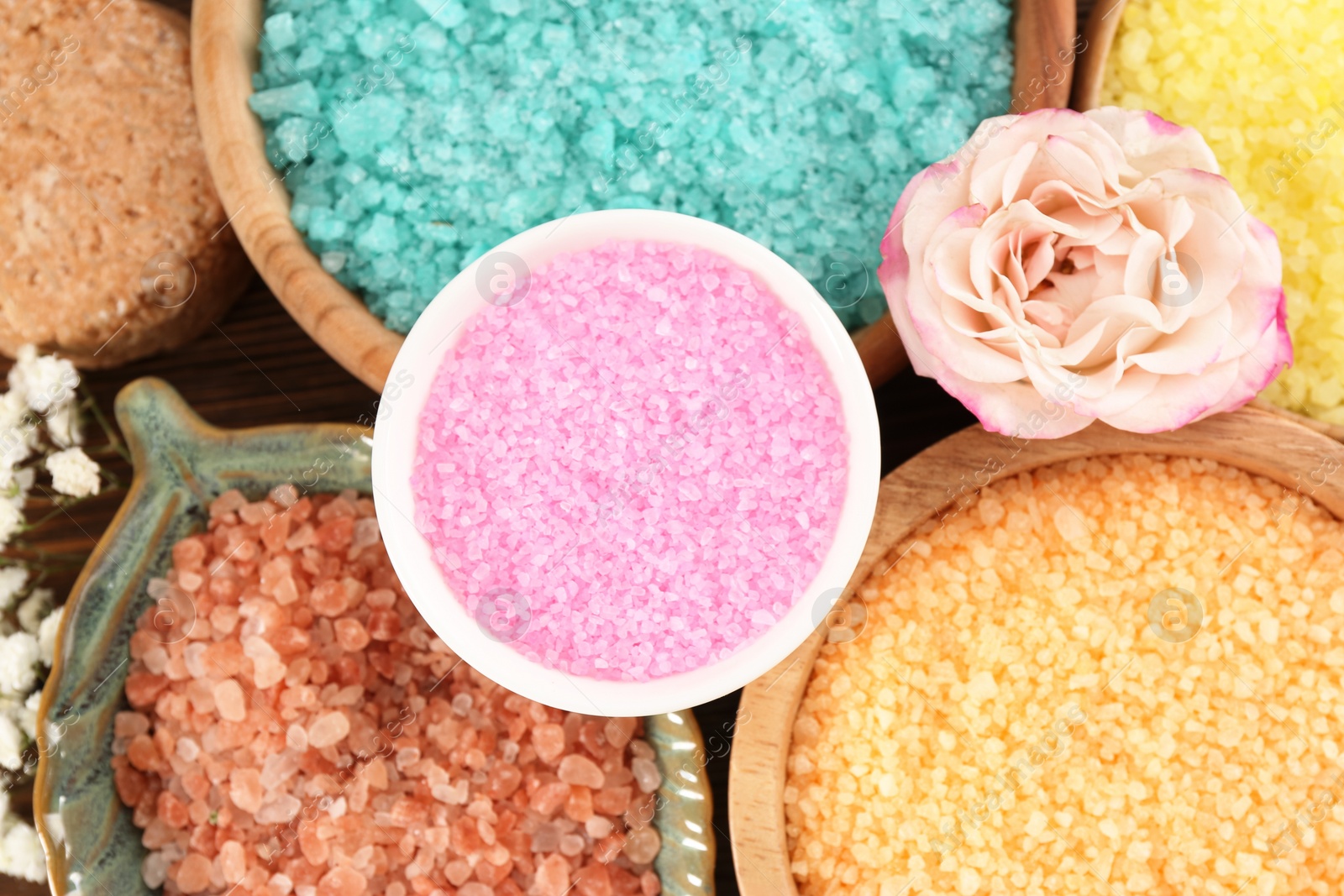 Photo of Bowls with sea salt and beautiful flowers on wooden table, flat lay