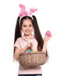 Photo of Little girl in bunny ears headband holding basket with Easter eggs on white background