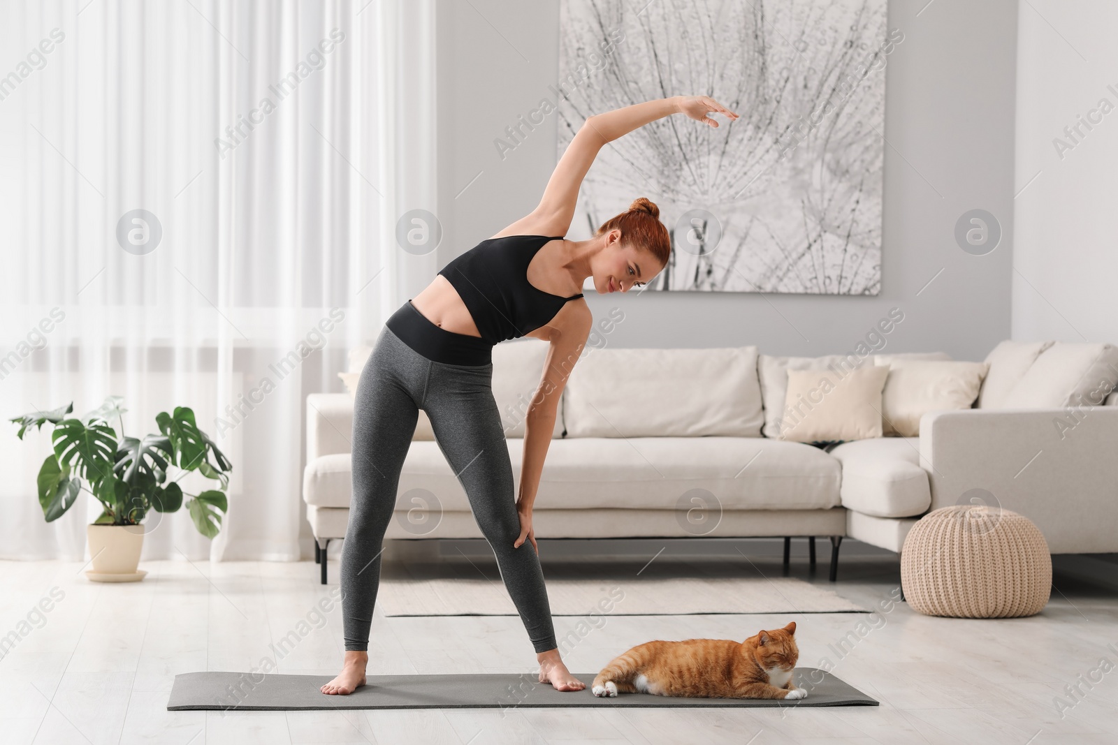 Photo of Beautiful woman with cute red cat practicing yoga on mat at home