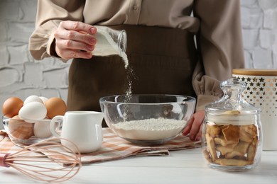 Woman adding baking powder into bowl at white wooden table, closeup