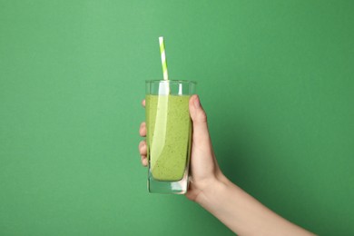 Photo of Woman holding glass of fresh smoothie on green background, closeup