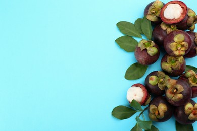 Photo of Fresh ripe mangosteen fruits with green leaves on turquoise background, flat lay. Space for text