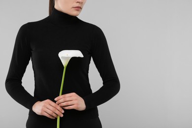 Photo of Woman with calla lily flower on light grey background, closeup and space for text. Funeral ceremony