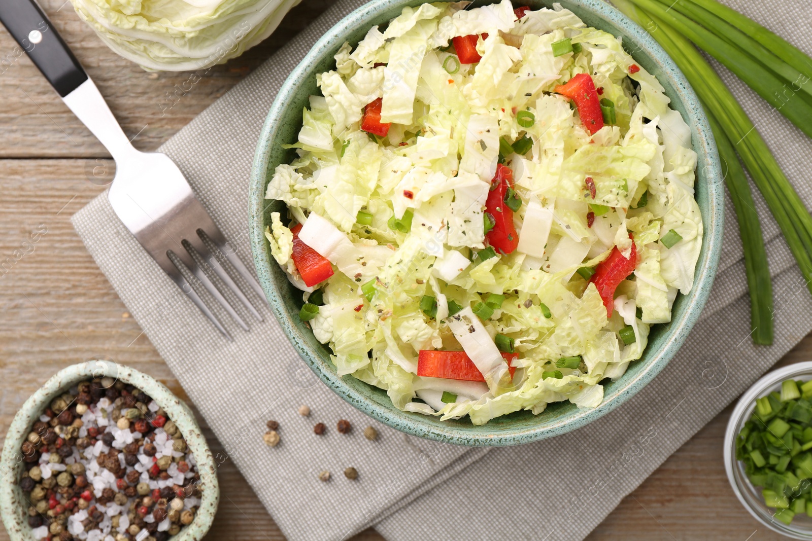 Photo of Tasty salad with Chinese cabbage in bowl and spices on wooden table, flat lay