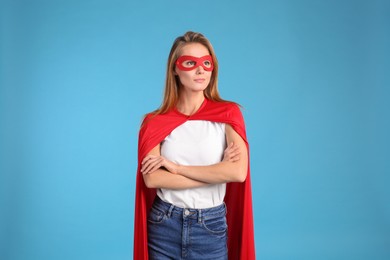 Photo of Confident woman wearing superhero cape and mask on light blue background