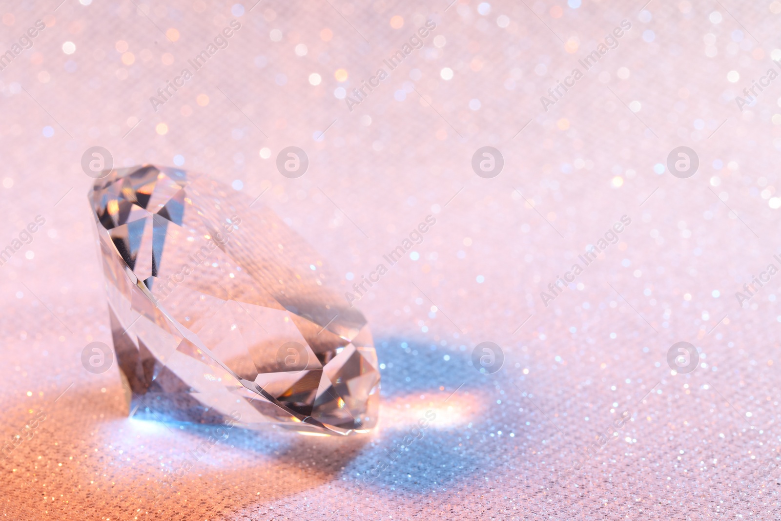 Photo of Beautiful dazzling diamond on pink glitter fabric, space for text