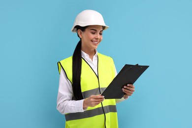 Engineer in hard hat holding clipboard on light blue background