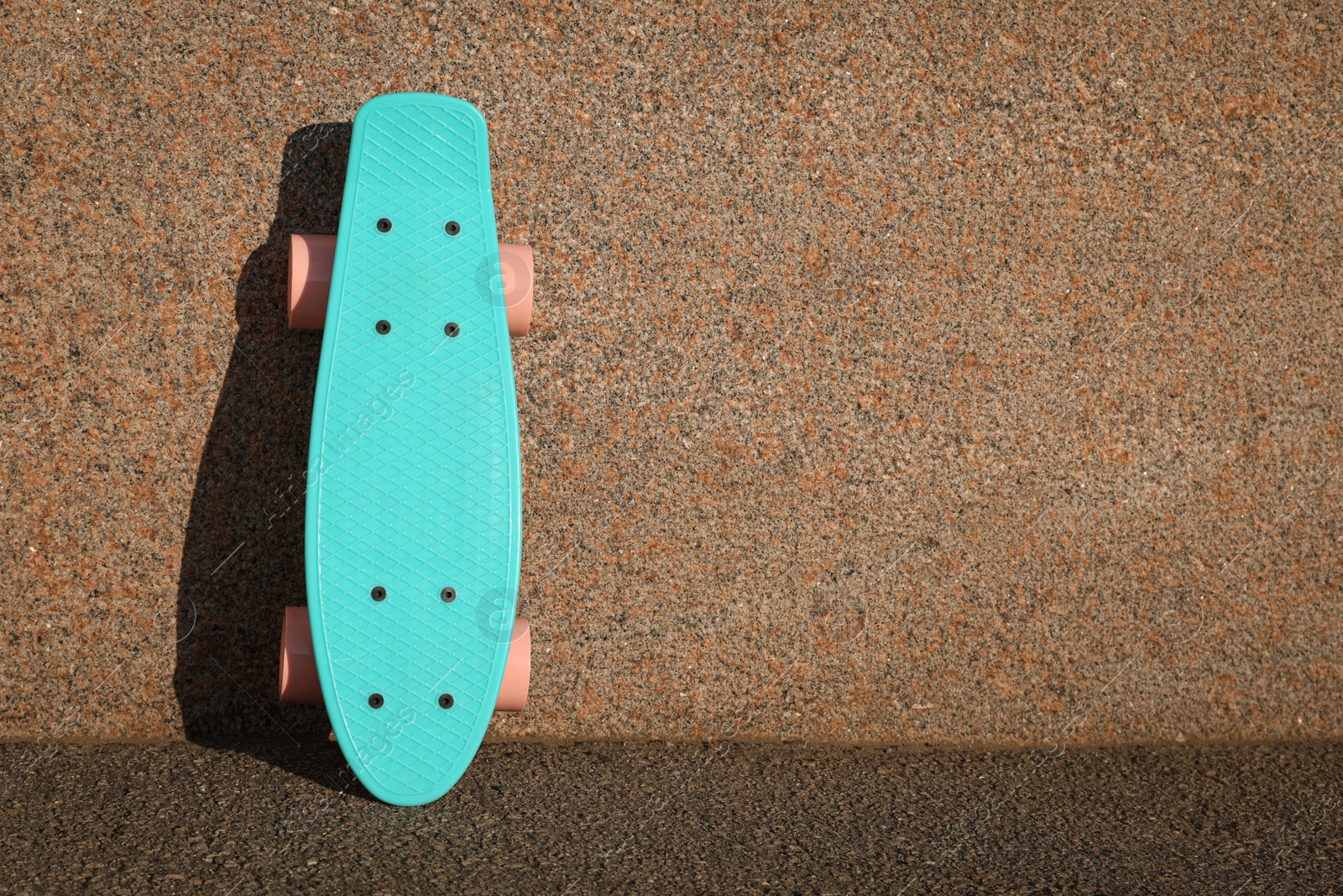 Photo of Light blue skateboard with pink wheels near wall outdoors. Space for text