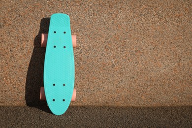 Photo of Light blue skateboard with pink wheels near wall outdoors. Space for text