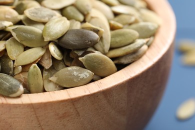 Wooden bowl with peeled pumpkin seeds on table, closeup
