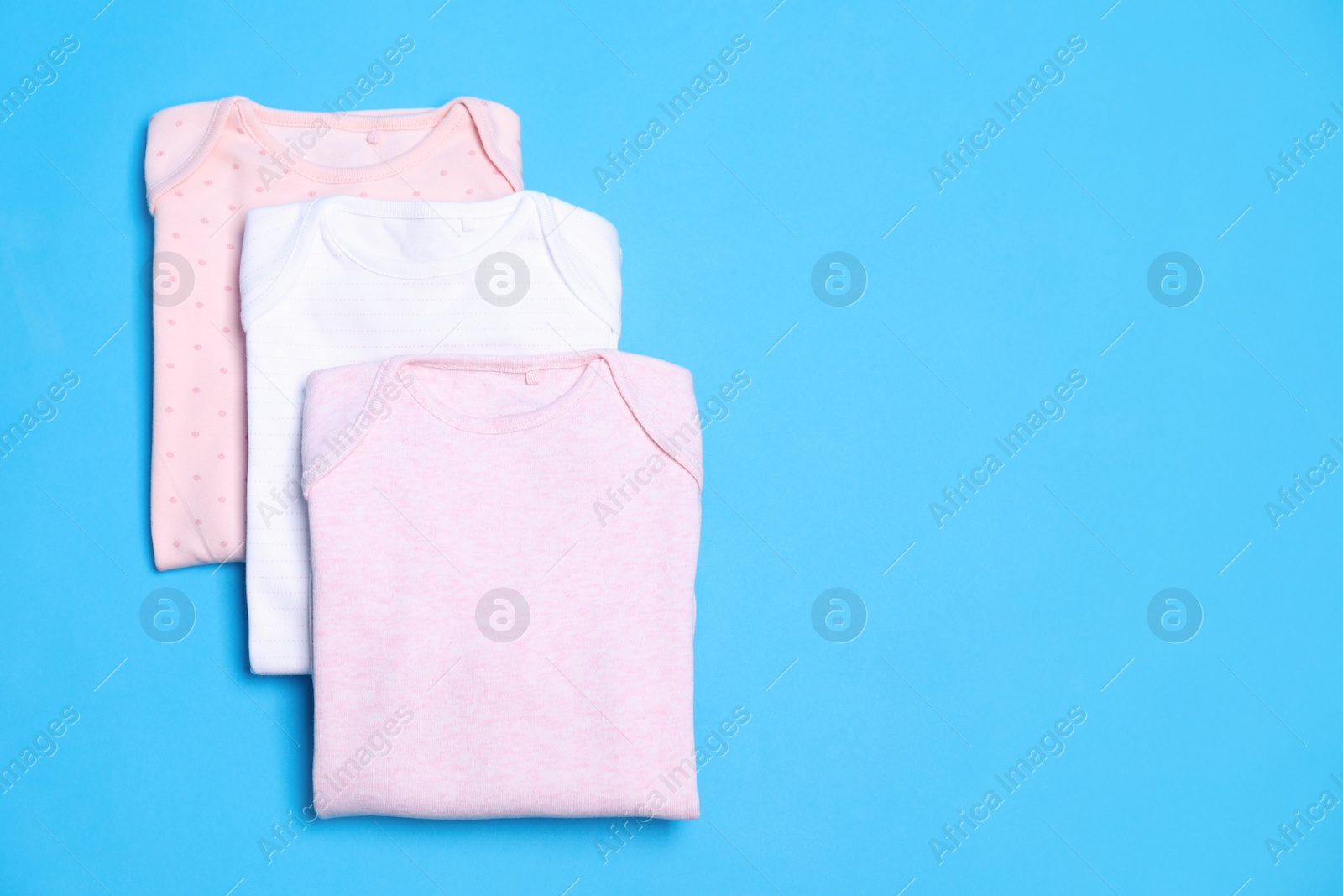 Photo of Folded baby bodysuits on blue background, flat lay. Space for text