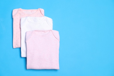 Photo of Folded baby bodysuits on blue background, flat lay. Space for text