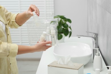 Photo of Woman packing cosmetic travel kit in bathroom, closeup and space for text. Bath accessories