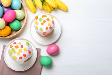 Photo of Easter cakes, color eggs and tulips on white wooden table, flat lay. Space for text