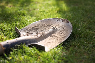 Photo of One dirty shovel on green grass outdoors, closeup