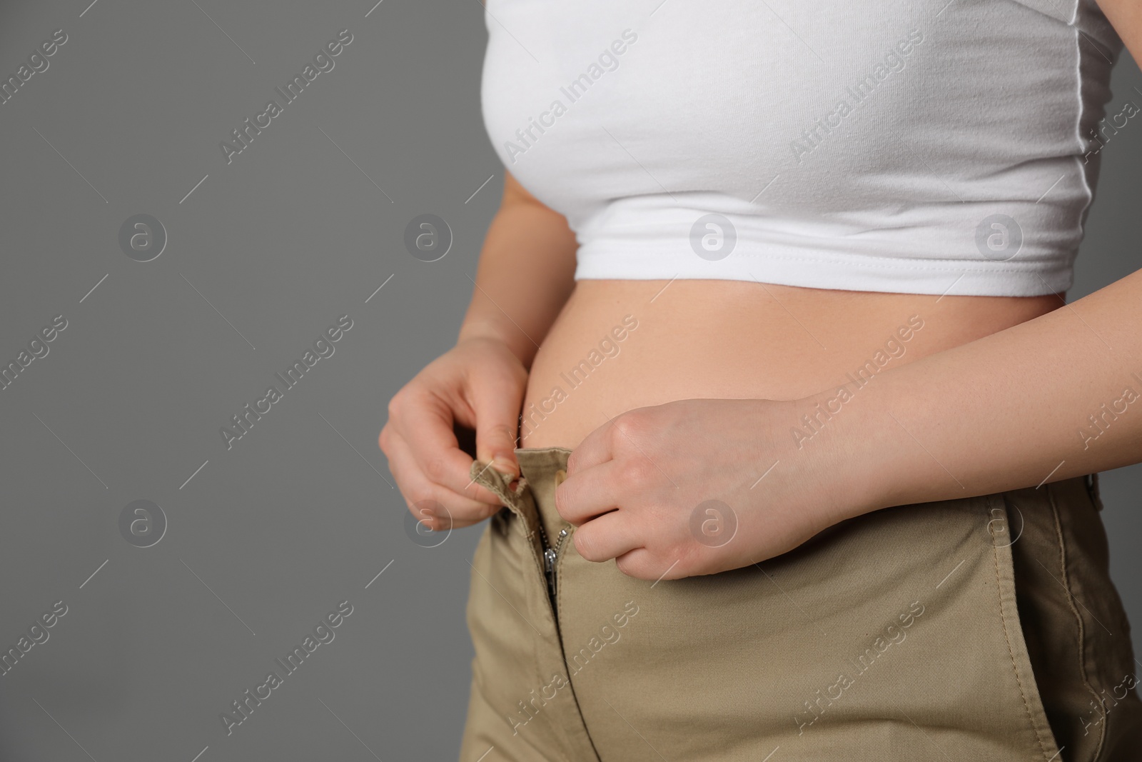 Photo of Overweight woman trying to button up tight pants on grey background, closeup. Space for text