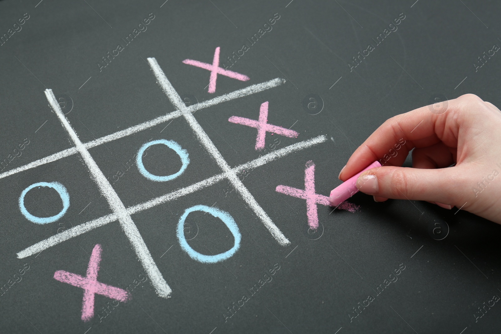 Photo of Woman playing tic tac toe on chalkboard, closeup