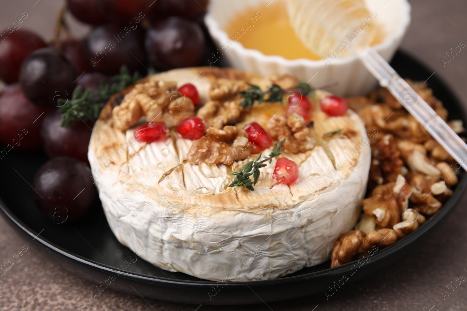 Photo of Plate with tasty baked camembert, honey, walnuts and pomegranate seeds on brown table, closeup