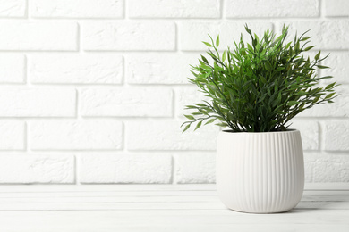 Photo of Beautiful artificial plant in flower pot on white wooden table near brick wall. Space for text