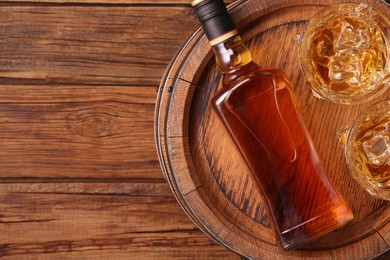 Photo of Whiskey with ice cubes in glasses, bottle and barrel on wooden table, top view. Space for text