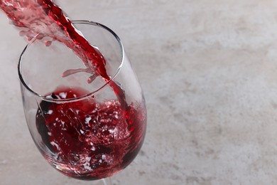 Photo of Pouring tasty red wine in glass at gray table, closeup. Space for text