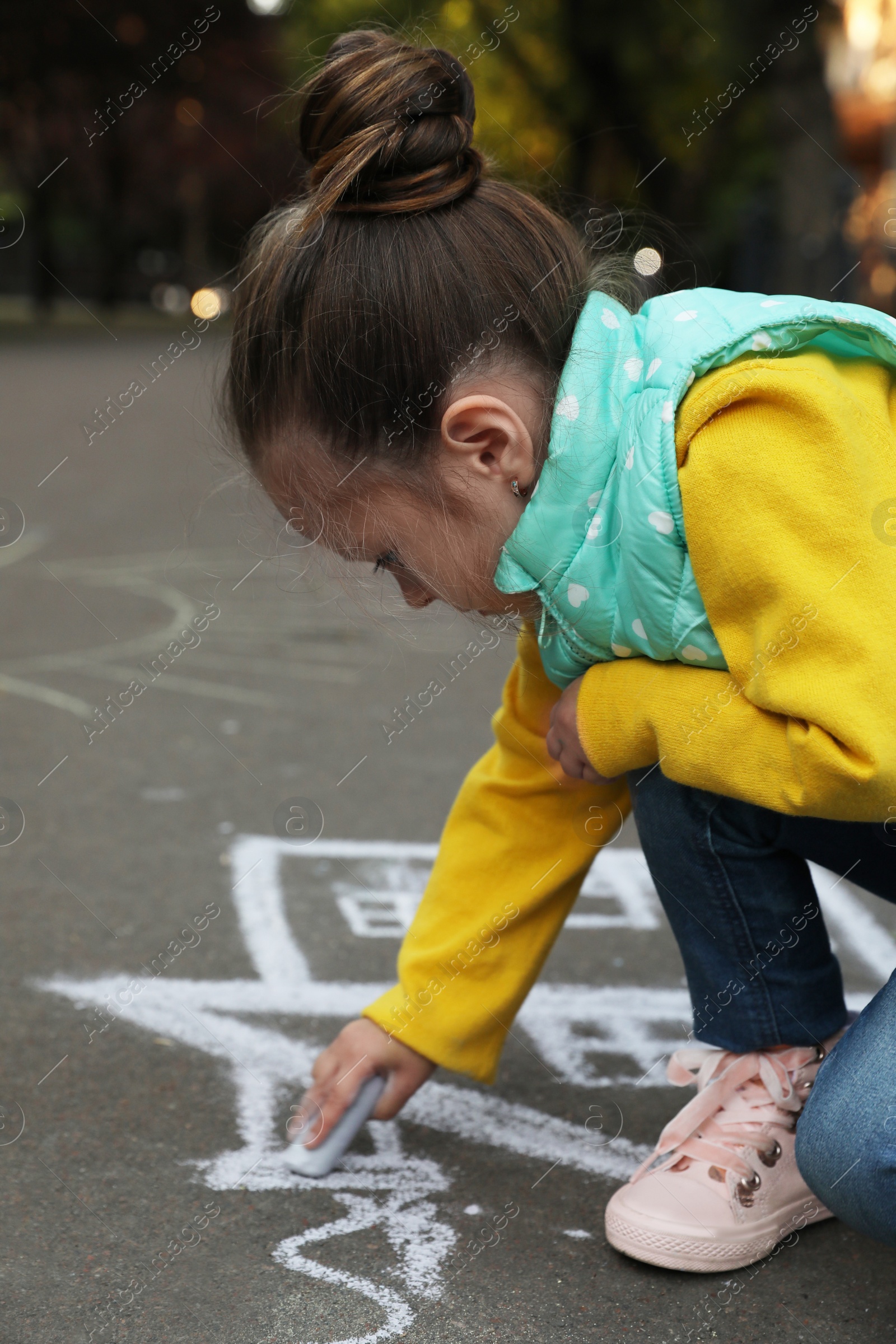 Photo of Child drawing house with chalk on asphalt