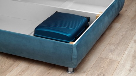 Photo of Storage drawer under bed with blue suitcase indoors