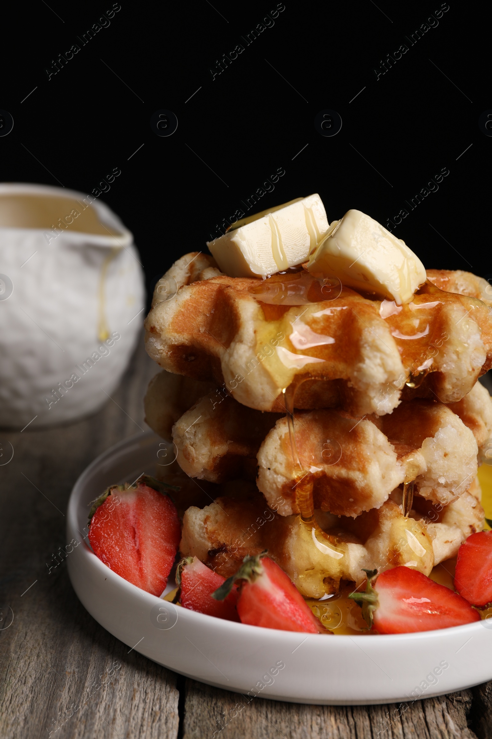 Photo of Delicious Belgian waffles with honey, butter and strawberries on wooden table, closeup