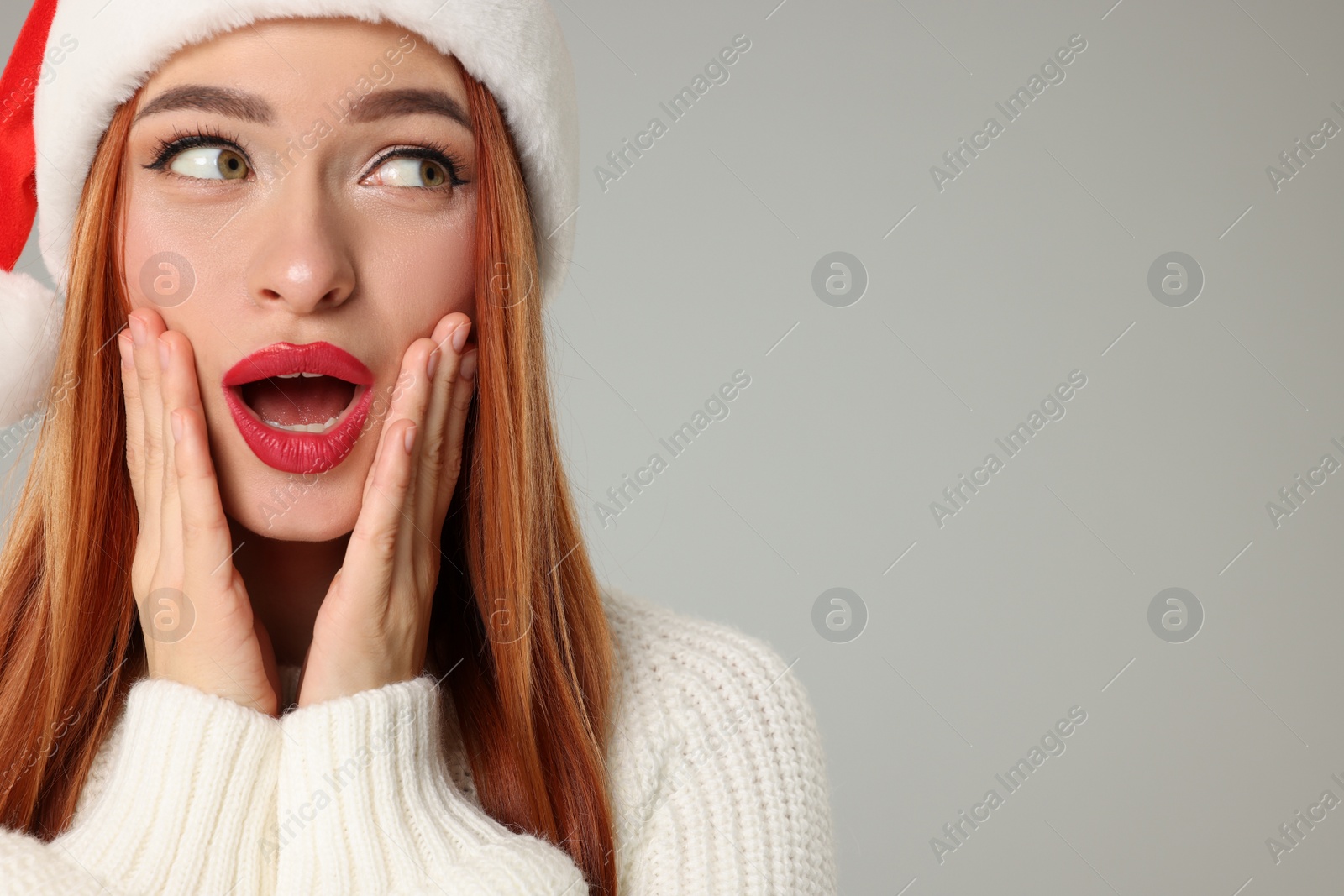 Photo of Young woman in Santa hat on light grey background, space for text. Christmas celebration