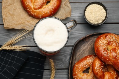 Tasty freshly baked pretzels and mug of beer on grey wooden table, flat lay