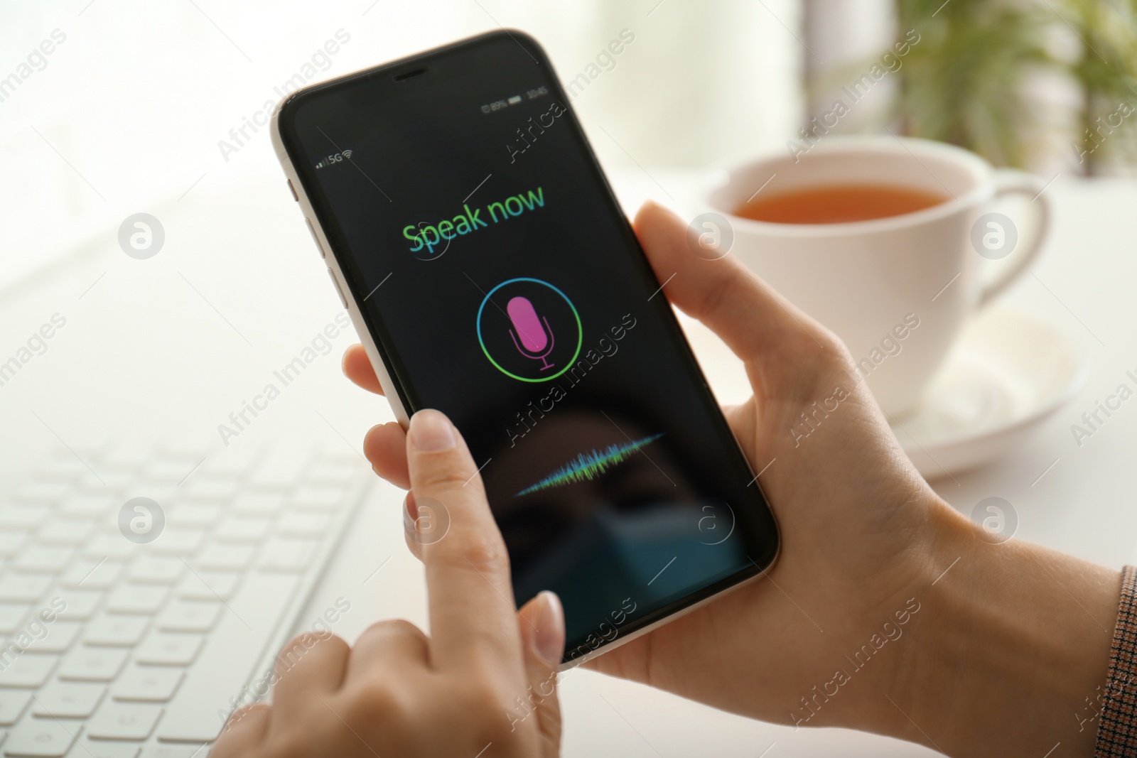 Photo of Woman using voice search on smartphone at white table, closeup