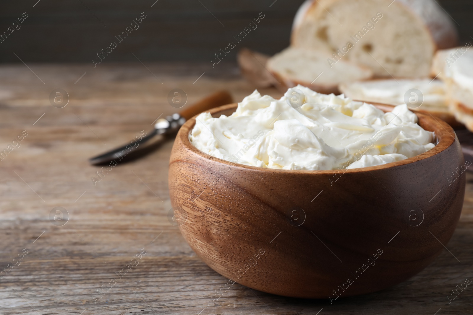 Photo of Bowl of tasty cream cheese and fresh bread on wooden table. Space for text