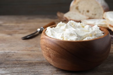 Bowl of tasty cream cheese and fresh bread on wooden table. Space for text