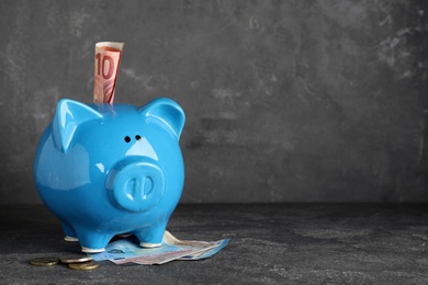 Blue piggy bank with money on grey table, space for text