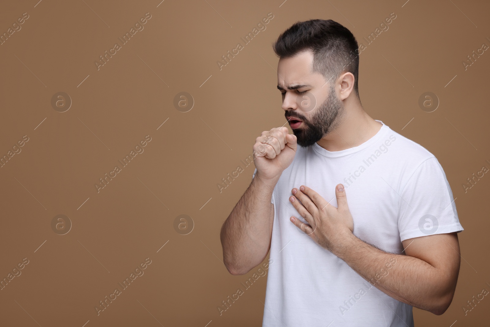 Photo of Sick man coughing on brown background, space for text