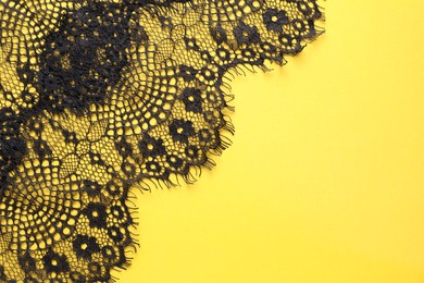 Photo of Black lace on yellow background, top view. Space for text