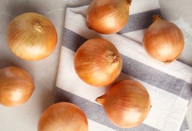 Photo of Ripe onions and fabric on grey table, flat lay