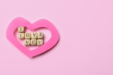 Photo of Phrase I Love You made of cubes and paper heart on pink background, flat lay. Space for text