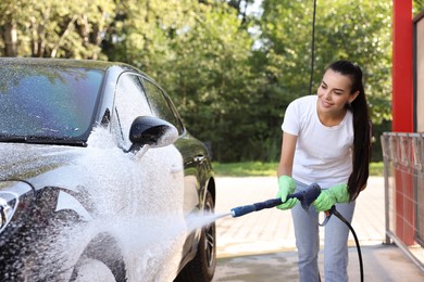 Photo of Happy woman covering automobile with foam at outdoor car wash