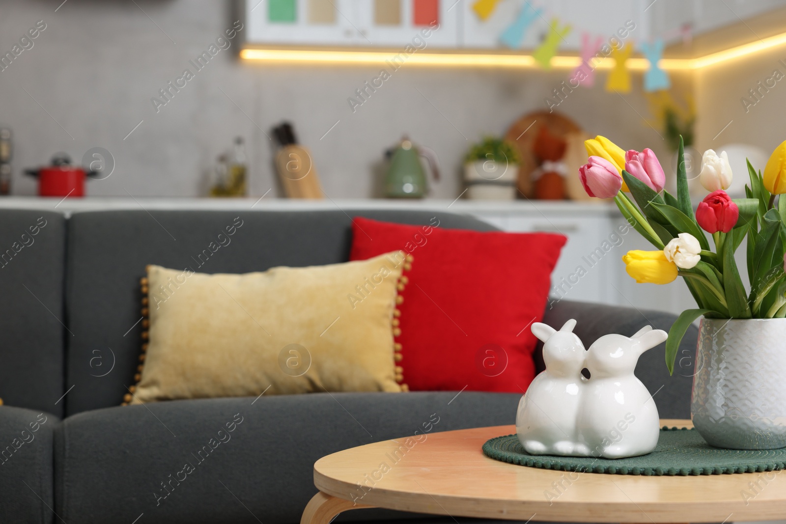 Photo of Easter decorations. Bouquet of tulips and bunny figures on table near sofa indoors. Space for text