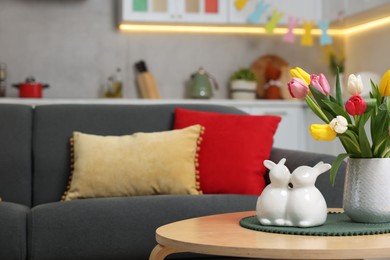 Photo of Easter decorations. Bouquet of tulips and bunny figures on table near sofa indoors. Space for text
