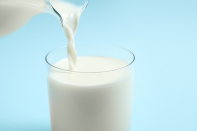 Photo of Pouring milk into glass on light blue background, closeup